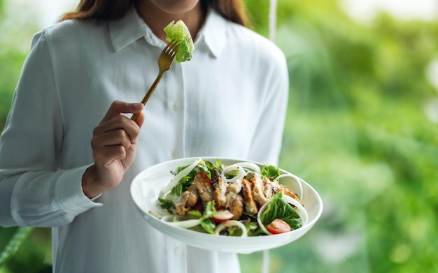 Image en gros plan d'une femme tenant et mangeant de la salade de poulet