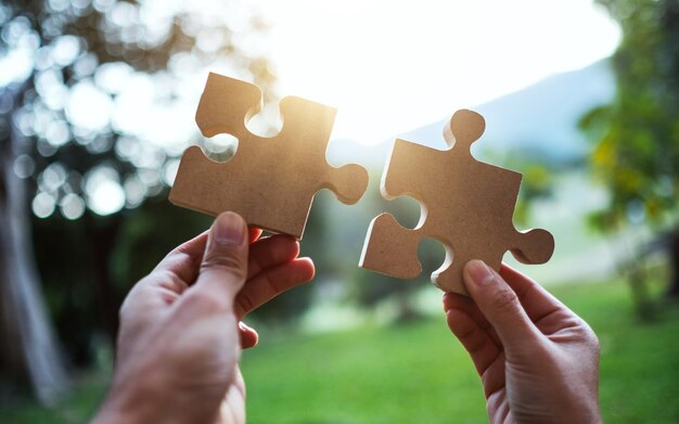 Image en gros plan d'une femme tenant et mettant un morceau de puzzle en bois ensemble à l'extérieur