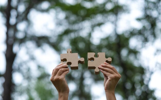 Image en gros plan d'une femme tenant et mettant un morceau de puzzle en bois ensemble à l'extérieur