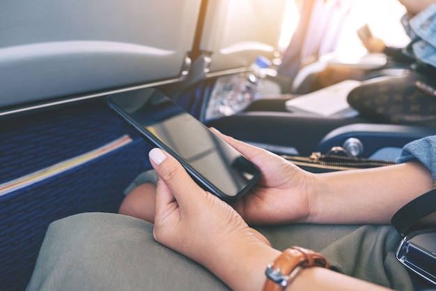 Image en gros plan d'une femme tenant un téléphone intelligent noir assis dans la cabine