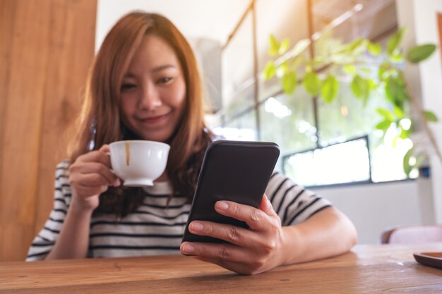 Image Gros Plan D'une Femme Tenant, Utilisant Et Regardant Un Téléphone Intelligent Tout En Buvant Du Café