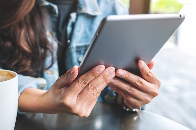 Image en gros plan d'une femme tenant et utilisant un tablet pc avec une tasse de café sur la table