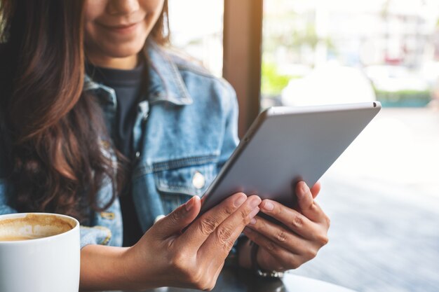 Image en gros plan d'une femme tenant et utilisant un tablet pc avec une tasse de café sur la table