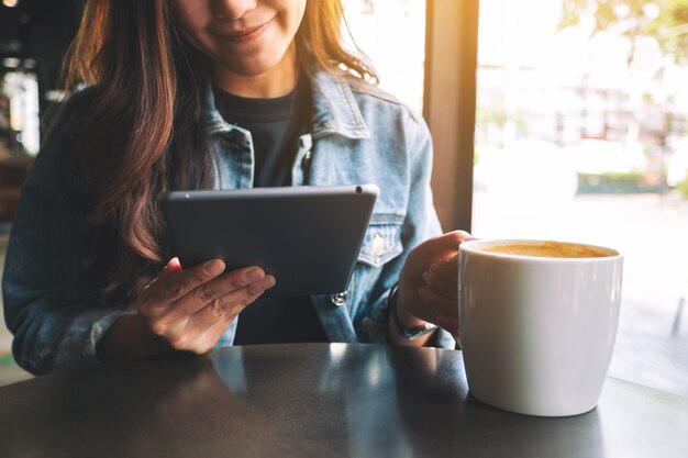 Image en gros plan d'une femme tenant et utilisant un tablet pc tout en buvant du café