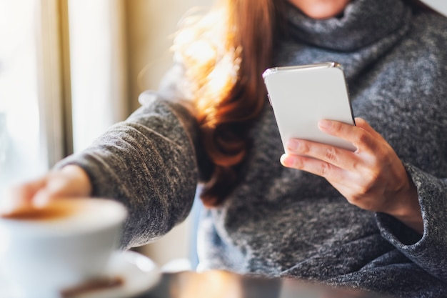 Image en gros plan d'une femme tenant et utilisant un téléphone portable tout en buvant du café au café