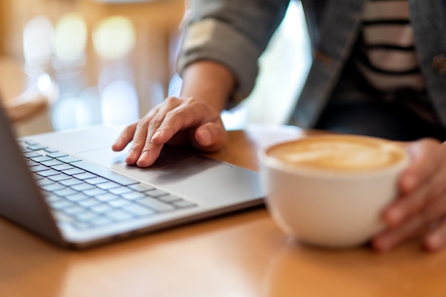 Image en gros plan d'une femme travaillant et touchant sur le pavé tactile d'un ordinateur portable tout en buvant du café