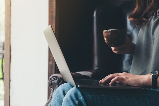 Image Gros plan d'une femme travaillant, utilisant et tapant sur le clavier d'un ordinateur portable tout en buvant du café