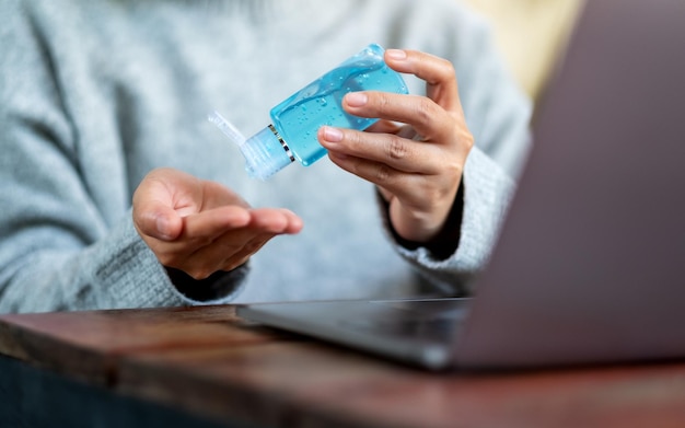 Image en gros plan d'une femme utilisant et appliquant un gel d'alcool pour se nettoyer les mains tout en travaillant sur un ordinateur portable à la maison pour le concept de virus de la santé et du Covid-19 ou 2020