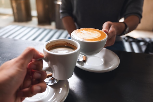 Image en gros plan d'un homme et d'une femme faisant tinter des tasses à café blanches dans un café