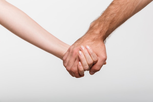 Image en gros plan d'un homme et d'une femme se tenant la main isolés sur un mur blanc.