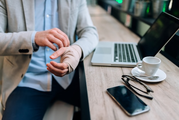 Image gros plan d&#39;un homme avec une main bandée assis dans le café devant un ordinateur portable.