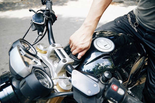 Image en gros plan d'un homme ouvrant le réservoir d'huile de moto pour le remplir d'essence