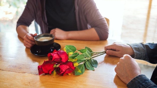 Image en gros plan d'un homme tenant et donnant des roses rouges à une femme à un rendez-vous au café