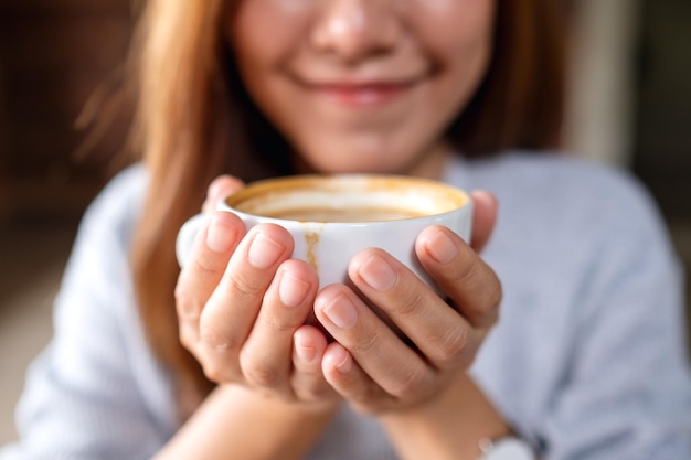 Image en gros plan d'une jeune femme asiatique sentant et buvant du café chaud