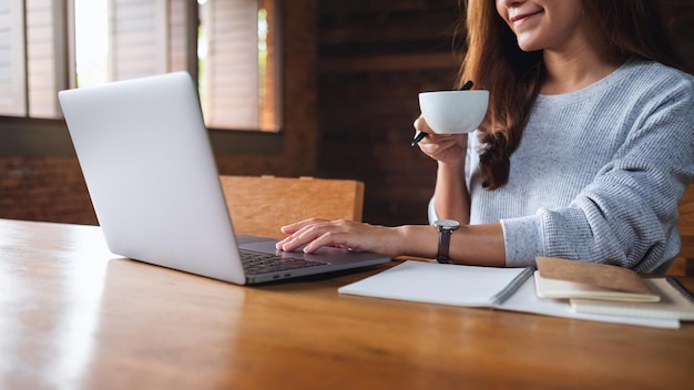 Image en gros plan d'une jeune femme buvant du café tout en travaillant sur un ordinateur portable