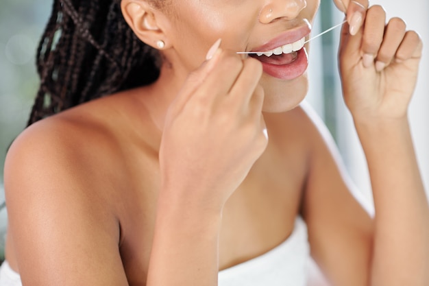 Image en gros plan de jeune femme noire à l'aide de soie dentaire après avoir pris une douche du soir