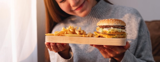 Image en gros plan d'une jeune femme tenant et mangeant un hamburger et des frites