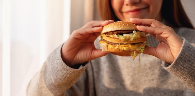 Image en gros plan d'une jeune femme tenant et mangeant un hamburger