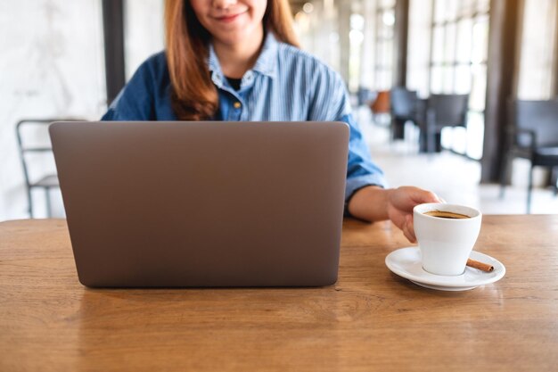 Image en gros plan d'une jeune femme utilisant et travaillant sur un ordinateur portable tout en buvant du café au café