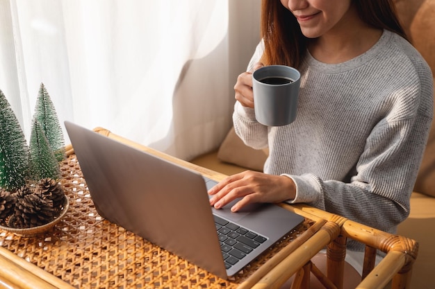 Image en gros plan d'une jeune femme utilisant et travaillant sur un ordinateur portable tout en buvant du café à la maison