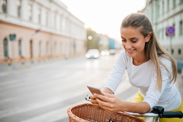 Image gros plan d&#39;une jeune fille souriante à l&#39;aide de téléphone en faisant du vélo dans la rue.