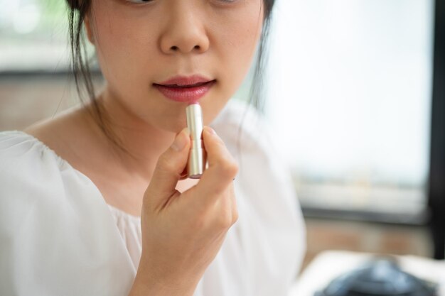 Image en gros plan d'une jolie femme asiatique appliquant du rouge à lèvres sur ses lèvres en se maquillant quotidiennement