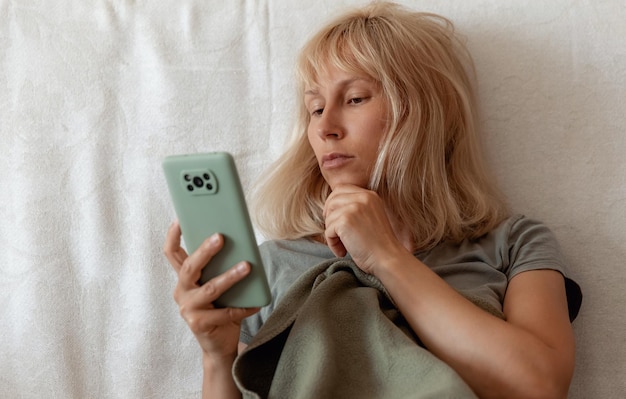 Image en gros plan d'une jolie femme assise à l'intérieur d'une maison confortable et utilisant un smartphone moderne mains féminines tapant un message texte via le concept de réseau social de téléphone portable