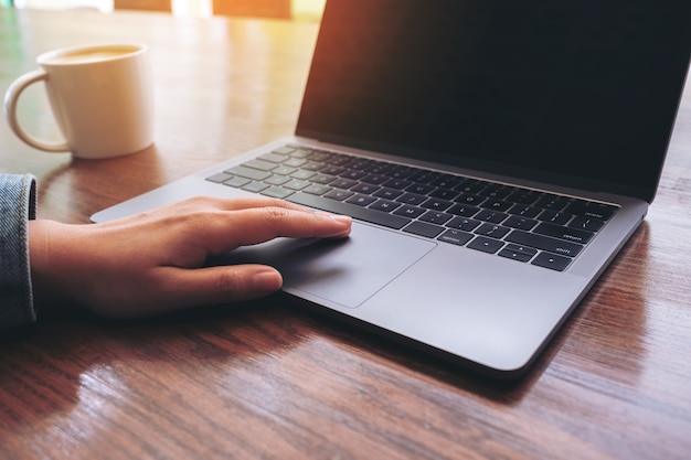 Image Gros plan d'une main à l'aide et en touchant le pavé tactile de l'ordinateur portable avec une tasse de café sur la table en bois