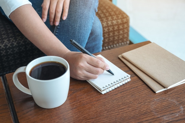 Image Gros plan d'une main de femme écrit sur un cahier vierge avec une tasse de café sur une table en bois