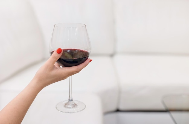 Une image en gros plan d'une main de femme tenant un verre de vin rouge avec un arrière-plan flou