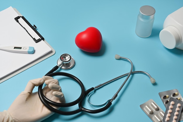 Image en gros plan d'une main de médecin avec un gant tenant un stéthoscope au-dessus de la table bleue