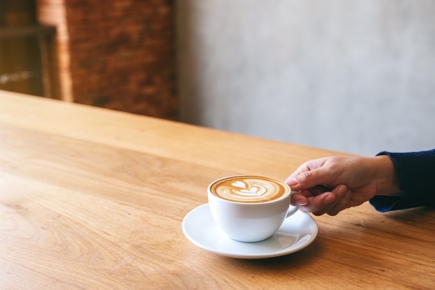 Image en gros plan d'une main tenant une tasse de café chaud sur une table en bois