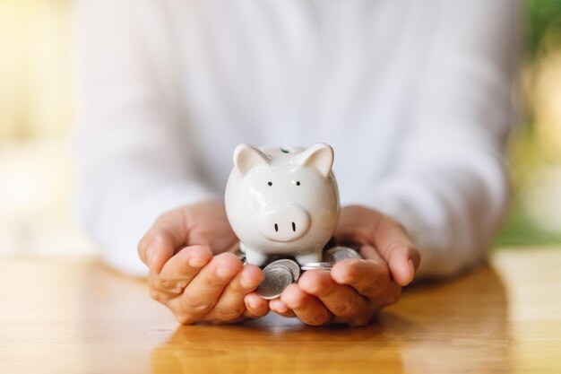 Image en gros plan des mains d'une femme tenant une tirelire et des pièces de monnaie pour économiser de l'argent concept