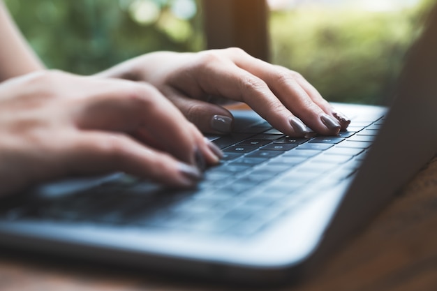 Image Gros plan des mains de femme travaillant et en tapant sur le clavier d'ordinateur portable sur une table en bois