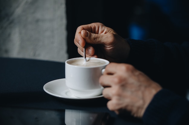 Image Gros plan des mains d'un homme d'affaires avec du café. Gros plan, mise au point sélectionnée de la main de l'homme tenant et remue le sucre dans une tasse de café blanc, concept de dent de relaxation.