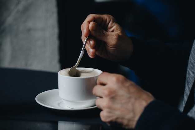 Image Gros plan des mains d'un homme d'affaires avec du café. Gros plan, mise au point sélectionnée de la main de l'homme tenant et remue le sucre dans une tasse de café blanc, concept de dent de relaxation.