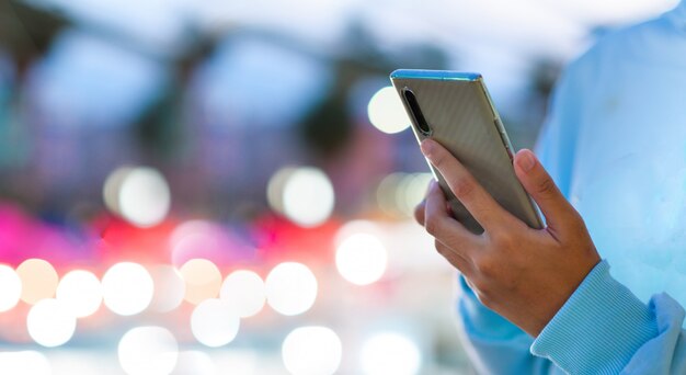 Image gros plan des mains masculines à l'aide de smartphone la nuit sur la rue commerçante de la ville, la recherche ou le concept de réseaux sociaux, hipster man tapant un message sms à ses amis