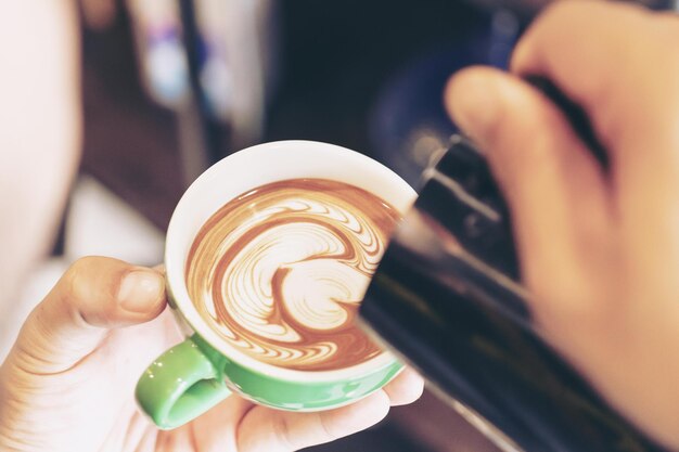 Image en gros plan des mains masculines Batista versant du lait faire du café latte art dans un café café