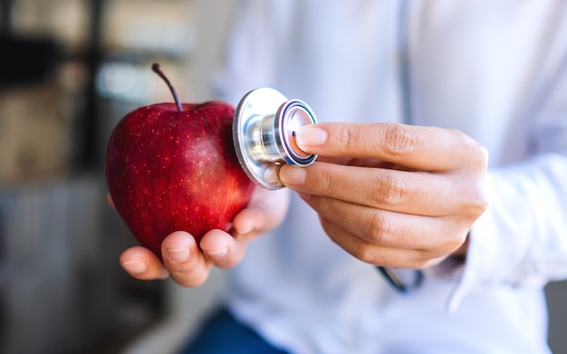 Image en gros plan d'un médecin utilisant un stéthoscope pour examiner une pomme rouge