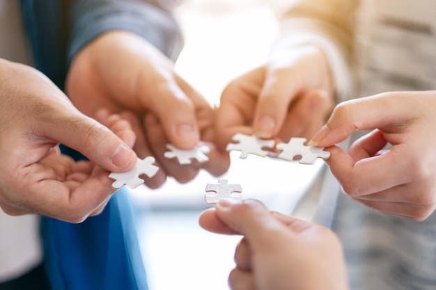 Image en gros plan de nombreuses personnes tenant et assemblant un morceau de puzzle blanc