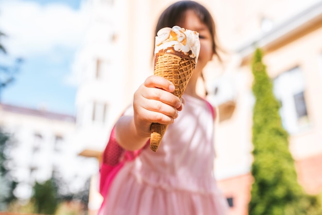 Image en gros plan d'une petite fille mignonne marchant le long de la rue de la ville et mangeant des glaces en plein air