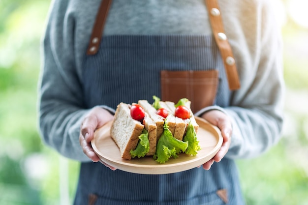 Image en gros plan d'une serveuse tenant et servant un sandwich au blé entier dans une assiette en bois