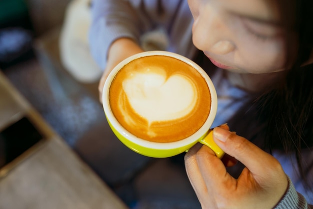 Photo image en gros plan d'une tasse de café en forme de cœur latte art jeune femme buvant du café dans le café