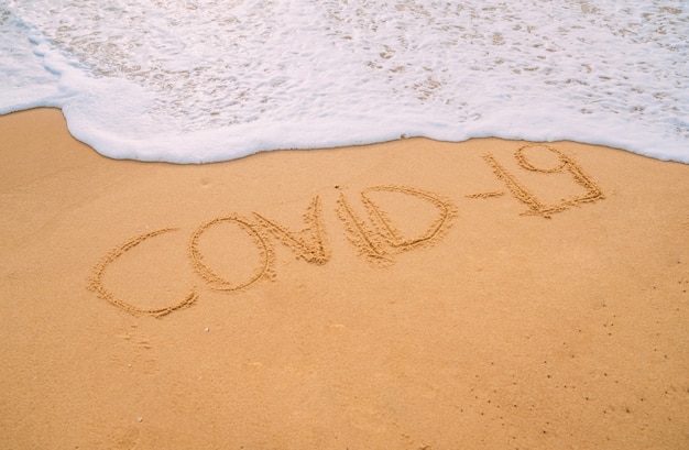 Image Gros plan des vagues de la mer laver le mot "covid-19" du sable sur la plage