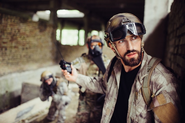 Une image de guerrier debout et penché contre le mur. Il regarde dehors. Guy est très prudent. Il montre le panneau d'arrêt à ses soldats. L'homme a un uniforme spécial et des lunettes sur le front.