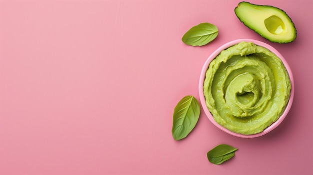 Image de haut d'un bol de trempette d'avocat frais sur une surface rose avec des feuilles de basilic