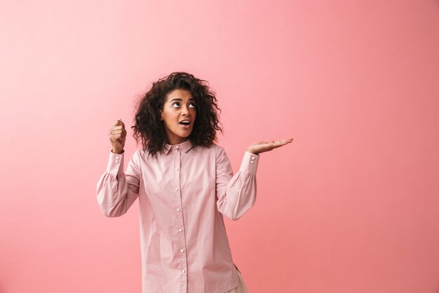 Image d'une heureuse belle jeune femme africaine posant isolé montrant copyspace imaginez qu'elle tenant un parapluie.