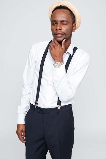 Image d'un homme africain réfléchi portant un chapeau qui pose en studio. Isolé sur fond blanc. Regardez la caméra.