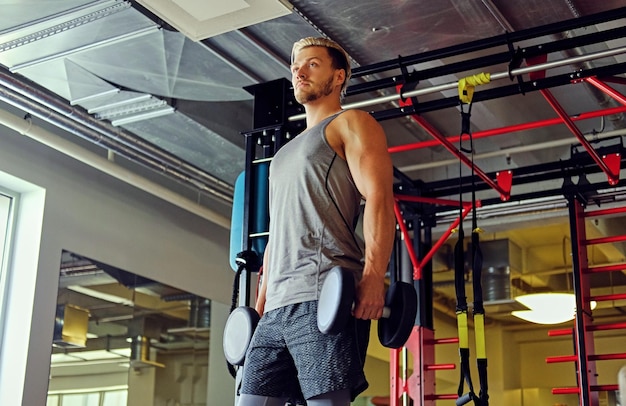 Image d'un homme athlétique complet du corps faisant des squats avec des haltères dans un club de gym.