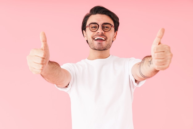 Image d'un homme joyeux brune portant des lunettes à la recherche et gesticulant les pouces vers le haut isolé